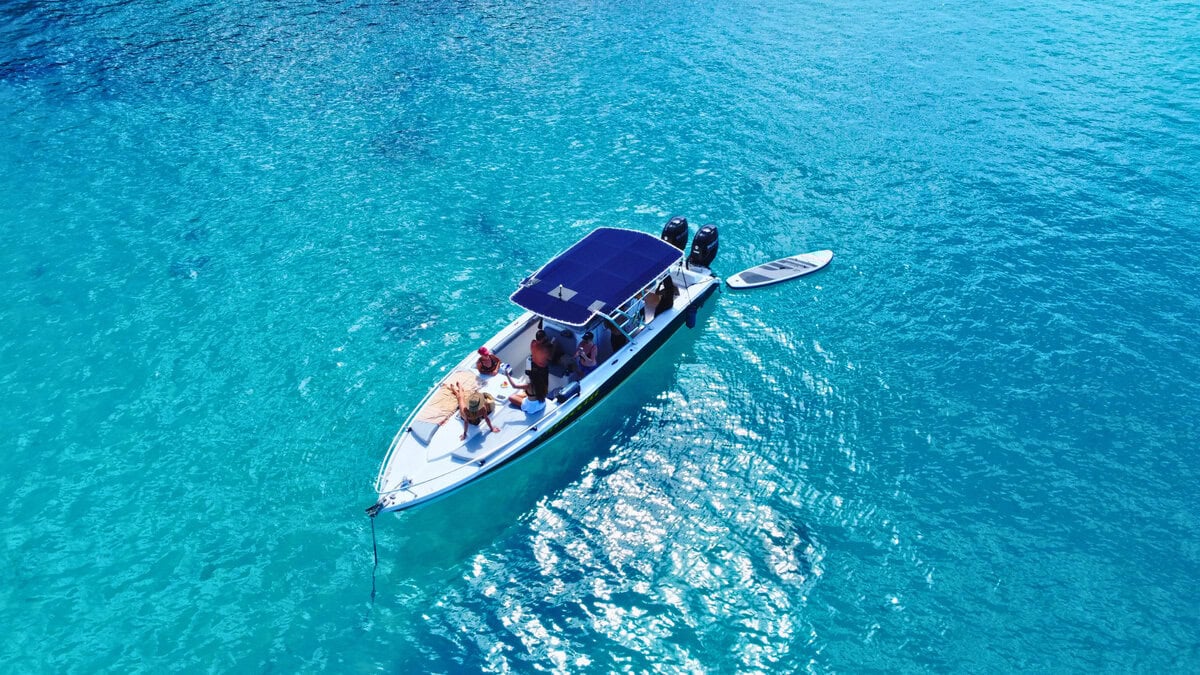 Gäste entspannen an Bord eines privaten Motorboots, das in klarem türkisfarbenem Wasser vor Anker liegt