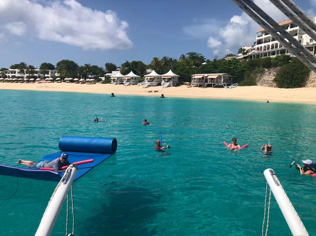 Gäste schwimmen neben einem privaten Katamaran an einem sandigen karibischen Strand