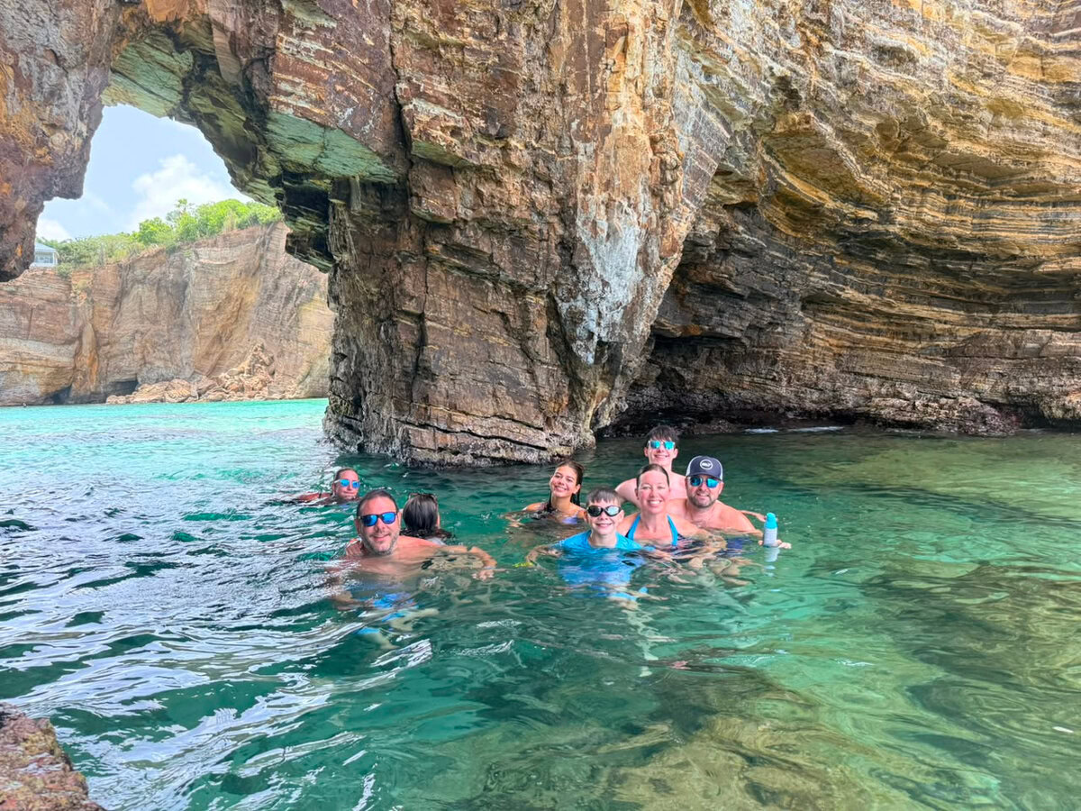 Familie und Freunde schwimmen neben einem natürlichen Felsbogen im Meer während eines privaten Bootscharters in St. Martin